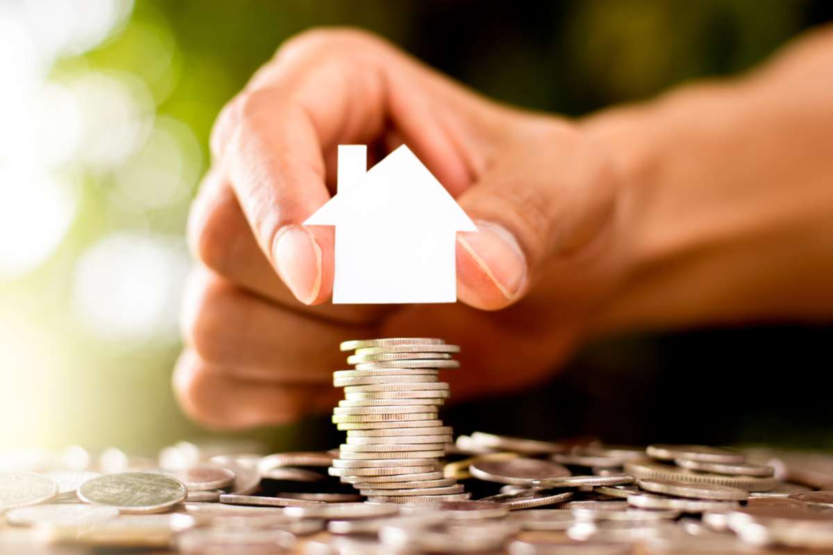 A hand places a small white house cutout on a stack of coins, property management companies Charleston, SC, concept